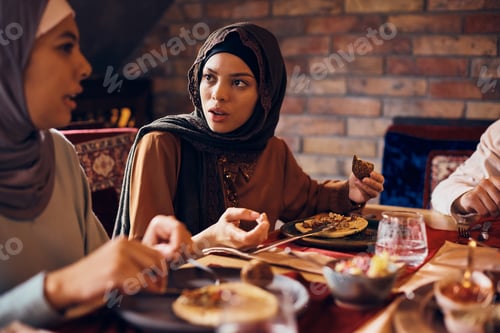 Preview: Young Muslim woman talking to her friends during lunch at dining table.