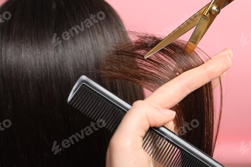 Preview: Hairdresser cutting client's hair with scissors on pink background, closeup