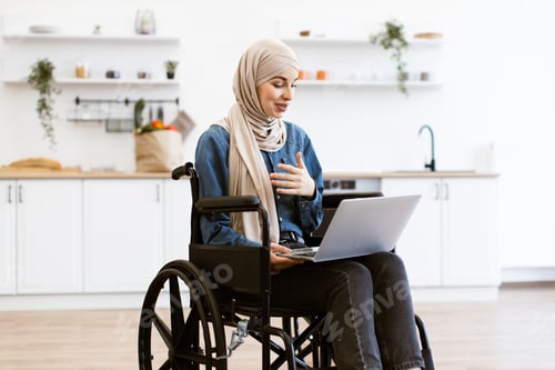Preview: Muslim woman in wheelchair working from home on laptop