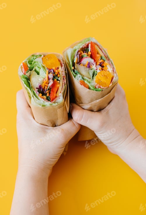 Preview: Vertical shot of a veggie wrap cut in half in hands on a yellow background