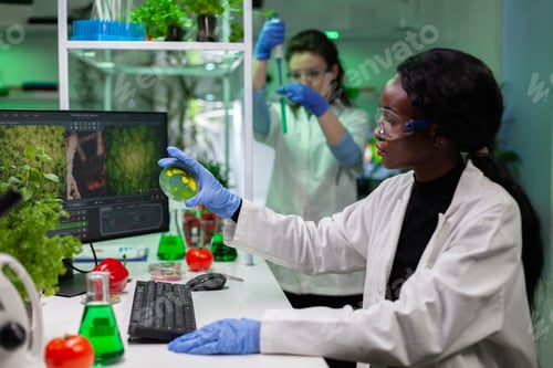 Preview: African american microbiologist researcher holding petri dish with liquid bacteria