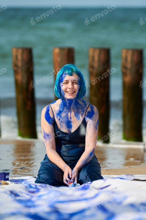 Preview: Artistic blue-haired woman performance artist in dress smeared with blue gouache paints on her body