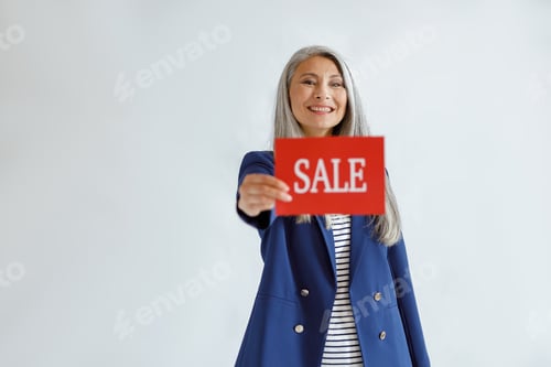 Preview: Beautiful Asian woman with loose grey hair shows red card with word Sale on light background