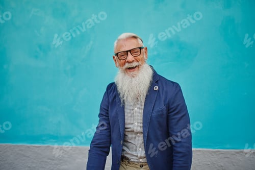 Preview: Older caucasian hipster man with prescription glasses and beard smiles happy outdoors in the city