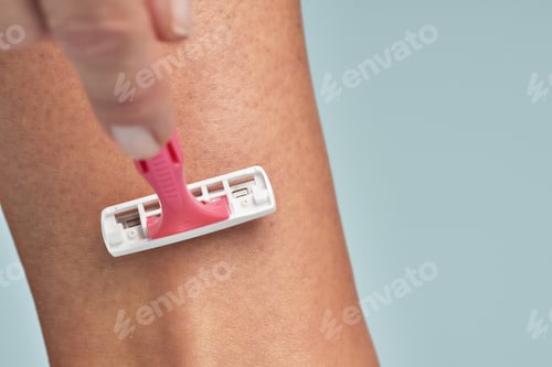 Preview: Close up shot of a woman shaving her leg with safety razor isolated on blue