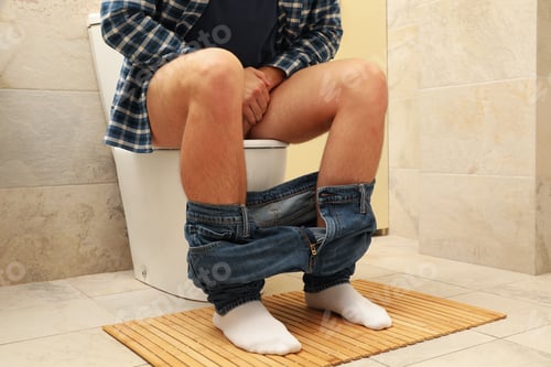 Preview: A man sits with his pants down on the toilet