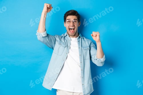 Preview: Excited handsome man triumphing, raising hands up and shouting for joy, celebrating victory