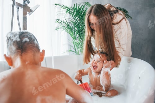 Preview: Having fun. Young mother helps her son and daughter. Two kids washing in the bath