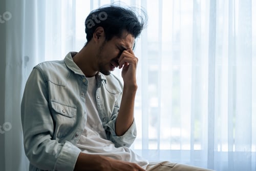 Preview: Asian young upset depressed man sitting alone in living room at home.