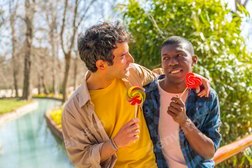 Preview: Multiethnic gay male couple eating a lollipop, lgbt concept, romantic fun
