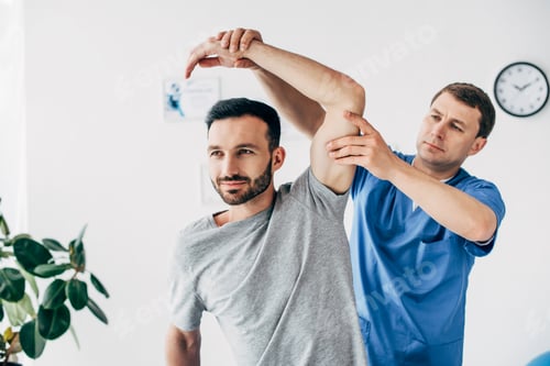 Preview: chiropractor stretching arm of handsome patient in hospital
