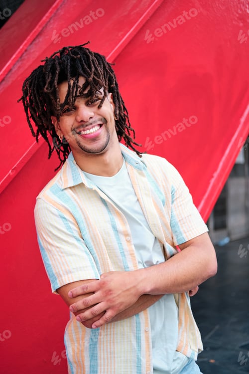Preview: young confident latinx man with curly hairlooking at camera and smiling