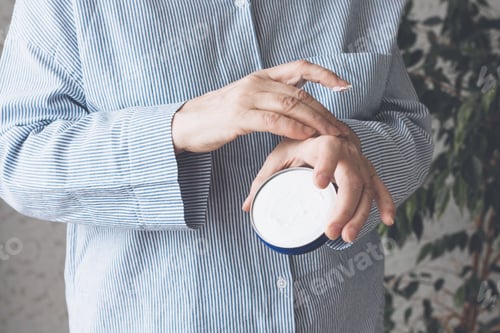 Preview: Woman in a blue shirt smears hands with cream