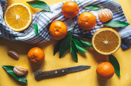 Preview: Fresh clementines, oranges on board with green leaves with a knife. Top view on a yellow background
