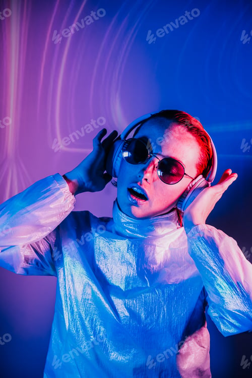 Preview: Portrait of sensitive dancing woman in sunglasses and headphones in neon light. Music lover.