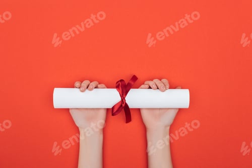 Preview: Cropped view of woman holding diploma with ribbon on red surface