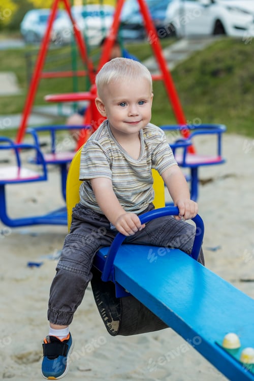Preview: Cute kid having fun on seesaw at playground. Concept of kindergarten. Vertical