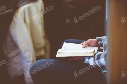 Preview: Closeup shot of a person reading a book and taking notes with a blurred background