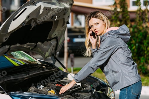 Preview: girl talking by smartphone and looking at camera while fixing broken car