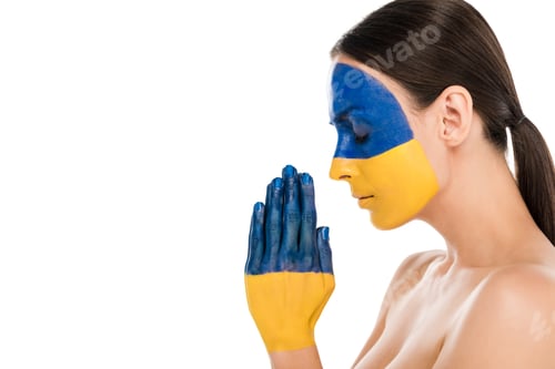 Preview: side view of naked young woman with painted Ukrainian flag on skin praying with closed eyes isolated