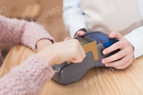 Preview: Close up of payment terminal on wooden surface and hands of girl with card