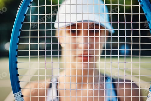 Preview: Closeup shot of a tennis racket with a sporty young woman standing in the background