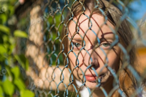 Preview: The girl in the park looks through a metal fence.