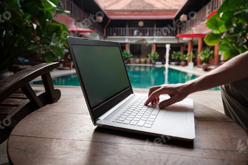 Preview: travel blogger sitting at swiming pool writing article on white laptop.