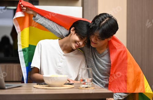Preview: Young gay couple under LGBTQ pride flag.