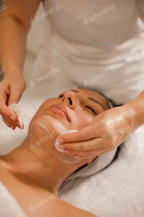 Preview: woman masseuse cleanses client's face before cosmetic facial massage