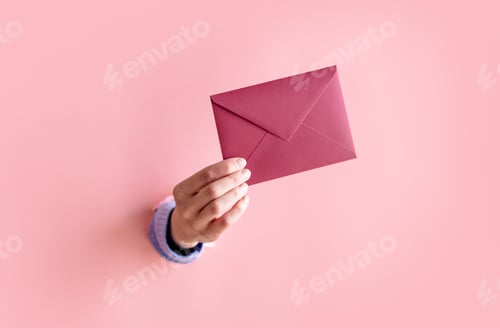 Preview: female hand hold red envelope on pink background.
