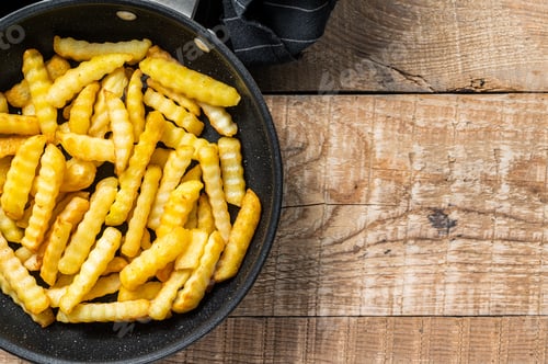Preview: Deep fried Crinkle French fries potatoes sticks in a pan. Wooden background. Top view. Copy space