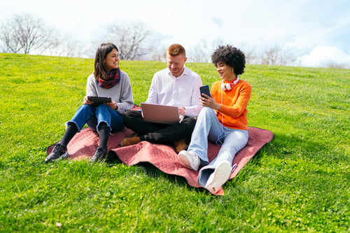 Preview: Students using laptop and tablet, relaxing on grass in park