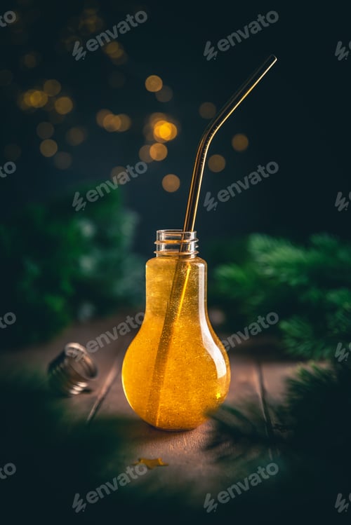 Preview: A light bulb with a golden liquid and a straw for a cocktail surrounded by fir branches, Christmas