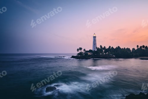 Preview: Illuminated lighthouse in the middle of palm trees. South coast of Sri Lanka at sunset.