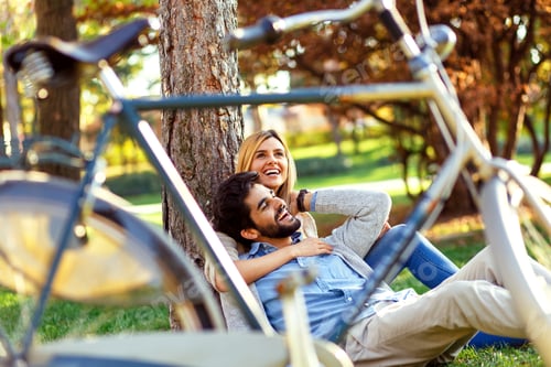 Preview: Young couple in love sitting in a autumn park leaning against a tree embracing one another.