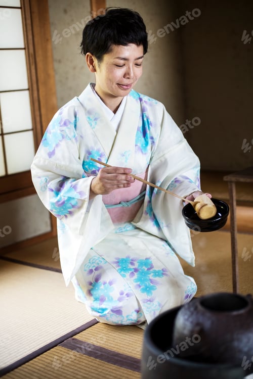 Preview: Japanese woman wearing traditional kimono kneeling on tatami mat during tea ceremony.