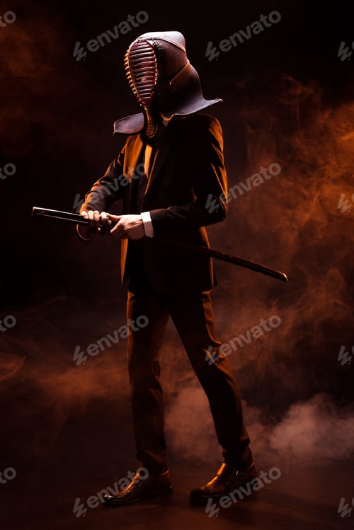 Preview: Full length view of kendo fighter in formal wear and helmet holding bamboo sword on dark