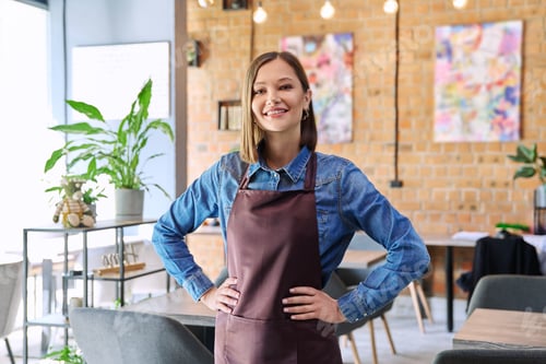 Preview: Young woman worker, owner in apron looking at camera in restaurant, coffee shop