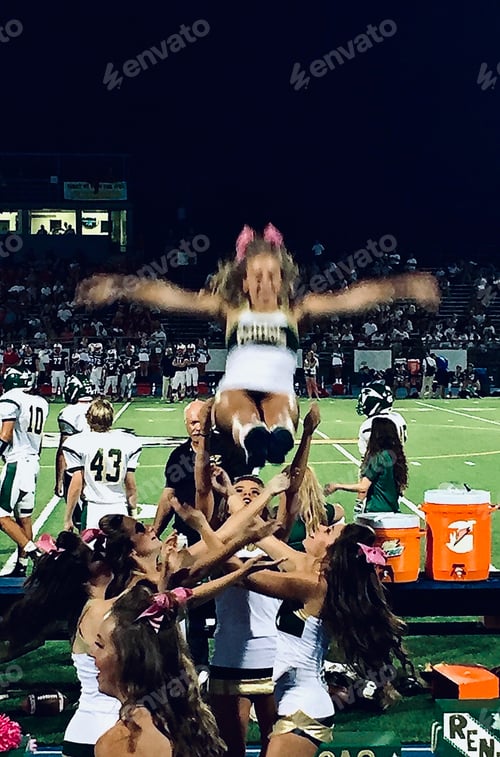 Cheerleaders Performing Stunt During Football Game at Night