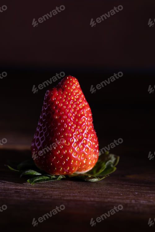 Preview: Large strawberry berry with green stipules on dark brown wooden background close-up with shadow