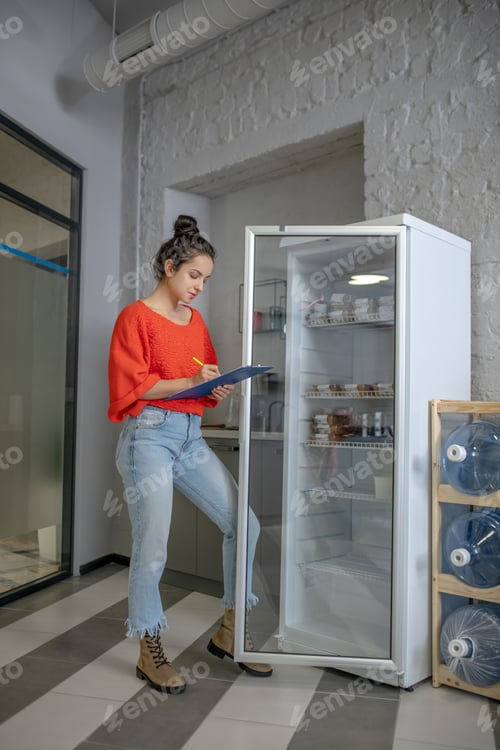 Preview: Young woman standing at the fridge, making notes