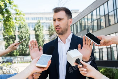 Preview: journalists interviewing serious businessman with microphones and smartphones