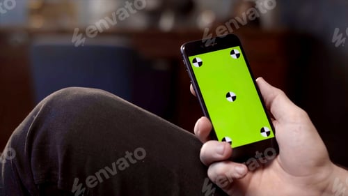 Preview: Man using mobile smartphone at home. Stock footage. Close up of a phone with a green screen in the