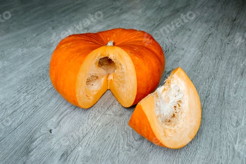 Preview: Orange pumpkin with a slice of it on a wooden surface