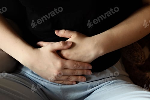 Preview: A woman holds her hands on her stomach while suffering from abdominal pain.