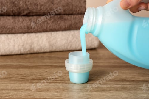 Preview: Woman pouring detergent into cap on table, closeup. Laundry day