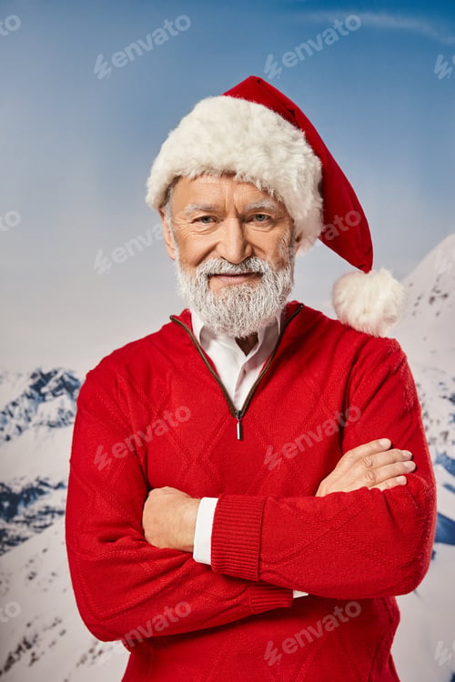 Preview: stylish Santa in red outfit posing with arms crossed on chest and looking at camera, winter concept