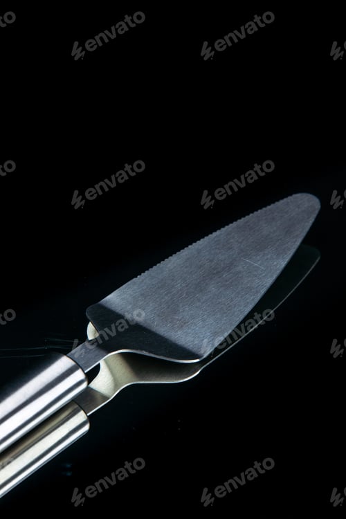 Preview: Close up view of stainless cake slicer lying on black background with free space