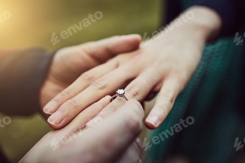 Preview: Cropped shot of a man putting an engagement ring onto his fiancees finger outdoors